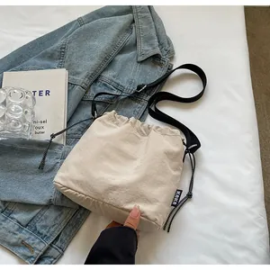 Détail du sac seau beige à cordon avec bandoulière noire et étiquette tissée latérale