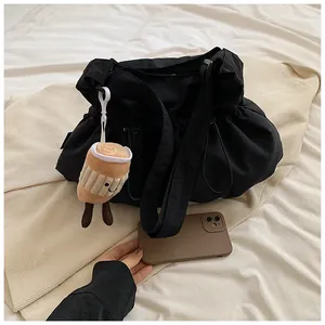 Detail of black drawstring bucket bag with cute plush coffee cup charm on fabric surface