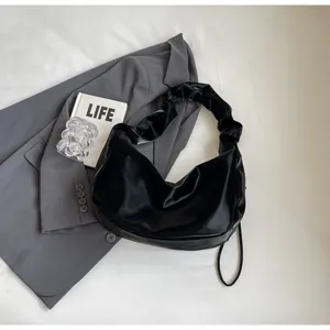 Close-up of black ruched shoulder bag with a glossy finish on a grey suit blazer