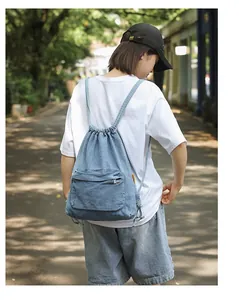 Sac à dos en jean bleu clair avec cordon et poche zippée porté par un mannequin dehors