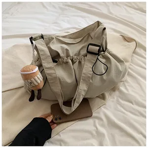 Detail of a large beige pleated drawstring bucket bag with a cute coffee cup plush charm