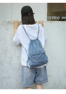 Détail du sac à dos en jean bleu clair à cordon sur un modèle avec poche extérieure