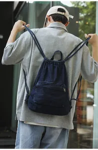 Gros plan d'un sac à dos en denim bleu avec cordon de serrage et poche zippée sur un modèle