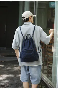 Détail du sac à dos en denim bleu avec cordon de serrage, poche zippée et sangle décontractée