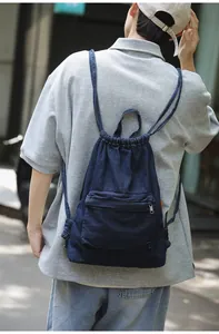 Détail du sac à dos en denim bleu foncé à cordon avec poche zippée sur le mannequin