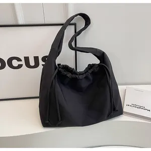 Dettaglio di una borsa a tracolla nera con coulisse su un tavolo bianco minimalista