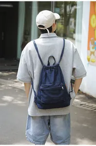 Sac à dos en jean bleu foncé avec cordon de serrage porté par un mannequin en extérieur