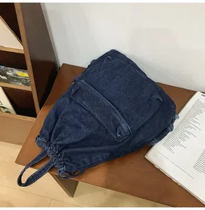 Vue détaillée du sac à dos en jean bleu foncé avec cordon et poche sur table en bois
