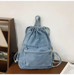 Vue détaillée de dessus du sac à dos en denim bleu clair avec cordon et poche zippée