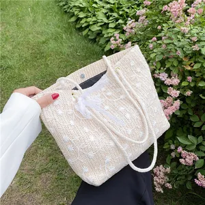 Stroh-Eimertasche mit Blumenstickerei und Spitzenband auf einem Rasenhintergrund