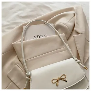 Dettaglio borsa a spalla in pelle bianca con fibbia a fiocco dorata su blazer beige