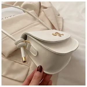 Dettaglio borsa a spalla in pelle bianca con logo a fiocco dorato e tracolla annodata