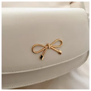 Dettaglio macro della borsa a spalla in pelle bianca con elegante fibbia a fiocco dorato