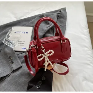 Close-up of wine red glossy handbag with pearl bow charm on gray blazer background