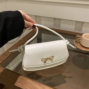 Dettaglio borsa a spalla in ecopelle bianca con fiocco in metallo dorato e tracolla annodata