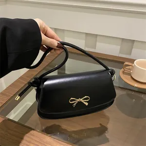Dettaglio borsa sottobraccio in pelle nera con chiusura a fiocco dorato in stile caffè
