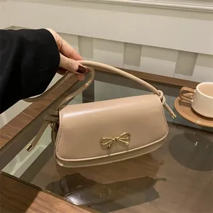 Dettaglio borsa beige sottobraccio con fiocco dorato e tracolla sottile in un ambiente