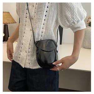 Detail of minimalist black saddle crossbody bag with smooth finish and adjustable strap
