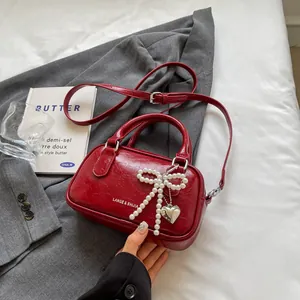 Silver bow-accented red bowling handbag with pearl charm and adjustable crossbody strap