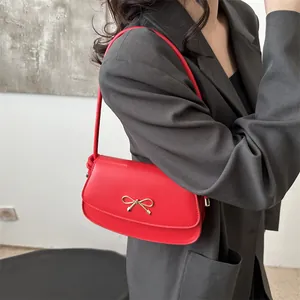 Dettaglio borsa a spalla in pelle rossa opaca con fiocco dorato su modella in abito grigio
