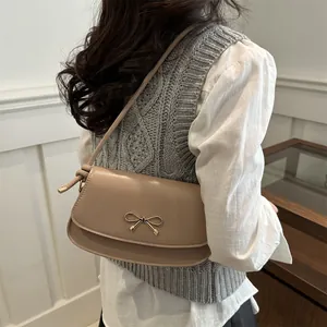 Dettaglio della borsa sottobraccio beige con fibbia a fiocco dorata sulla spalla