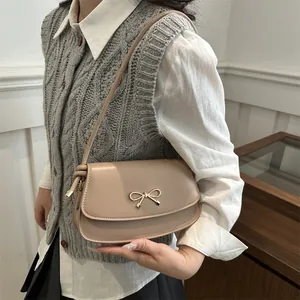 Dettaglio della borsa sottobraccio con fiocco dorato e tracolla annodata su modella