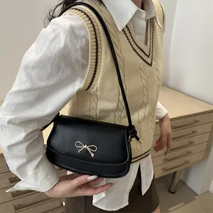 Dettaglio borsa a spalla in pelle nera con chiusura a fiocco dorato in stile collegiale