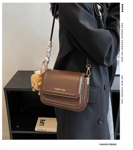 Close-up of brown leather crossbody bag with gold logo, decorative scarf and plush charm