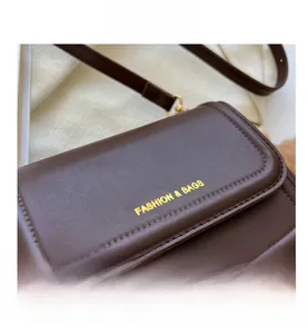 Detailed close-up of dark brown leather crossbody bag with golden fashion logo lettering