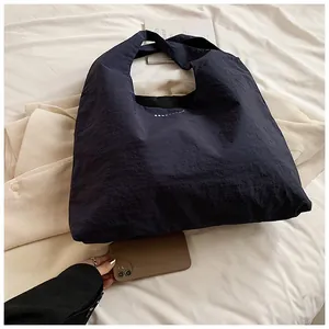 Detail of dark blue nylon tote bag showing wrinkled fabric texture and white logo