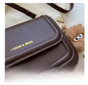 Detailed close-up of fine stitching on dark brown leather crossbody bag with gold text