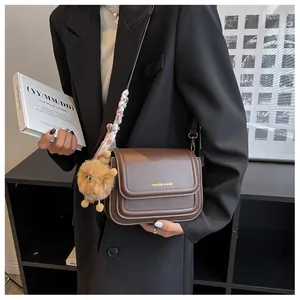 Brown leather crossbody bag detail with silk scarf and plush charm on black suit