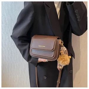 Detail of dark brown crossbody bag featuring gold logo and decorative scarf charm