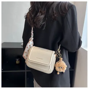 Detail of cream crossbody bag with fashion text, silk scarf strap, and plush charm