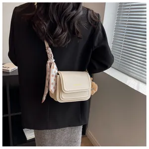 Cream crossbody bag detail with polka dot scarf and plush pompom charm on a model