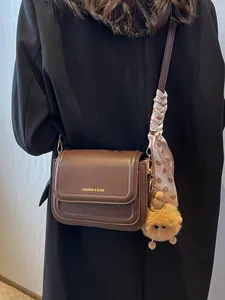 Minimalist brown leather crossbody bag with scarf and plush charm on black coat