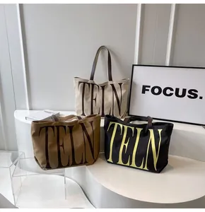 Trois sacs cabas minimalistes en toile en beige, marron et noir sur des marches