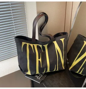 Détail d'un sac cabas en toile noire avec lettres jaunes et poignées en cuir marron foncé