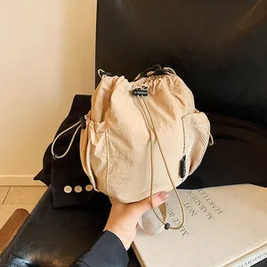 Minimalist beige nylon drawstring bucket bag with mesh side pockets and utility style
