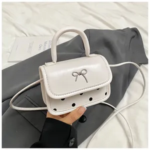Detailed close-up of cream mini bag with metallic bow and classic black polka dots
