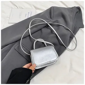Detail of trendy metallic silver mini crossbody bag placed on a grey blazer and white fabric
