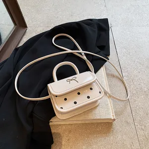 Chic mini crossbody bag with black polka dots and a metallic bow on creamy white leather