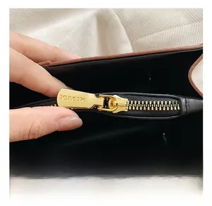 Detail of golden zipper on two-tone handbag showing interior brand engraving