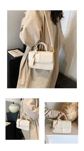 Detail view of cream-colored textured crossbody bag with gold buckle and fashion tag