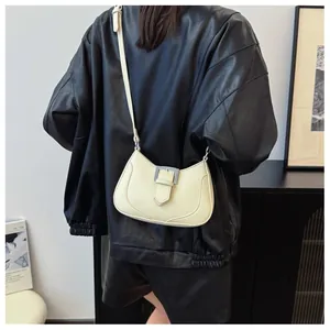 Détail du sac demi-lune crème avec boucle argentée porté sur une veste en cuir