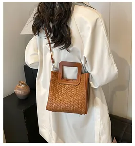 Détail d'un sac seau tressé marron avec des poignées rectangulaires en bois uniques