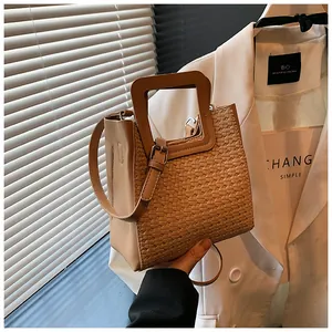Détail du tissage et de la poignée en bois carrée d'un sac seau beige porté main