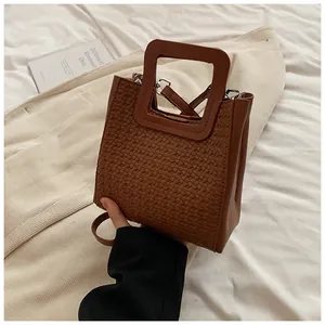 Détail d'un sac seau tressé marron avec des poignées carrées et une bandoulière amovible
