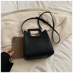 Gros plan d'un sac seau noir tressé avec poignée carrée et téléphone pour la taille