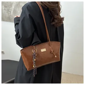 Close-up of a brown leather tote bag with a golden nameplate and woven rope ornament